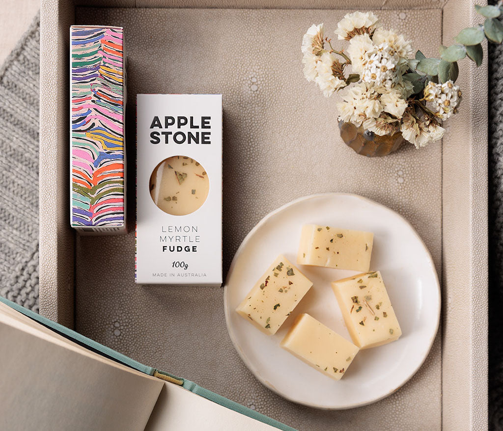 Apple Stone lemon myrtle fudge on a plate with packaging and flowers on a textured surface