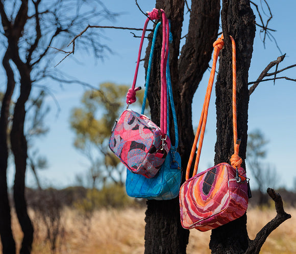 Quilted crossbody bag with Aboriginal artwork by Athena Granites from Warlulurlangu Artists. Features  a matching blue rope strap, shown on a solid white background.