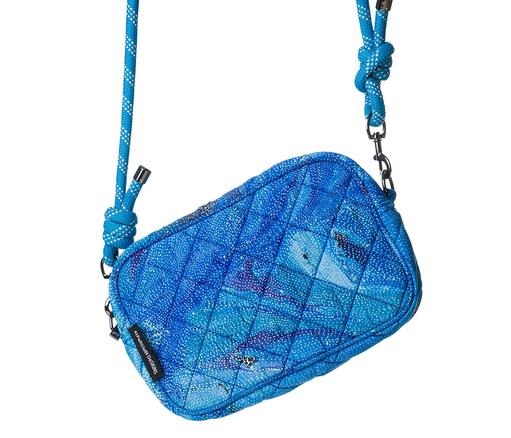 Quilted crossbody bag with Aboriginal artwork by Athena Granites from Warlulurlangu Artists. Features  a matching blue rope strap, shown on a solid white background.