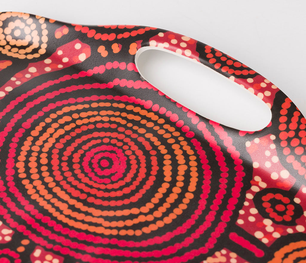A close up of a rectangular bamboo/melamine serving tray focusing on the handle, featuring Aboriginal artwork by Teddy Gibson from Warlukurlangu Artists. Image on a white background.
