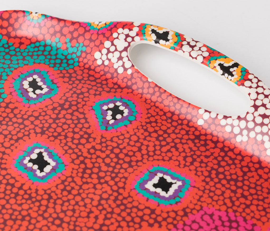 A close up of a rectangular bamboo/melamine serving tray focusing on the handle, featuring Aboriginal artwork by Ruth Stewart from Warlukurlangu Artists. Image on a white background.