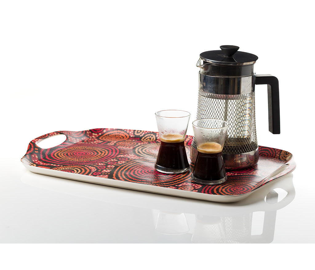 A rectangular bamboo/melamine serving tray with integrated side handles, featuring Aboriginal artwork by Teddy Gibson from Warlukurlangu Artists. A Coffee Plunger and two glass cups sit atop the tray. Image on a white background.