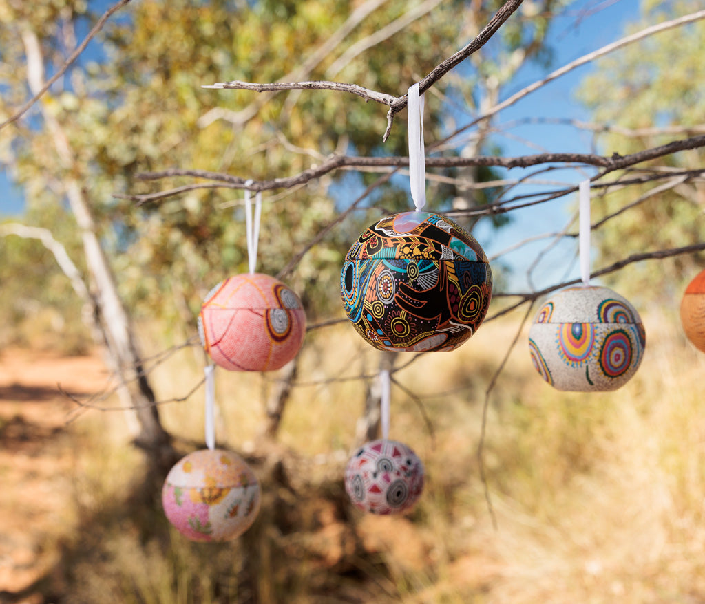 Aboriginal Art Christmas Bauble Tins hanging from a branch outdoors with a natural background