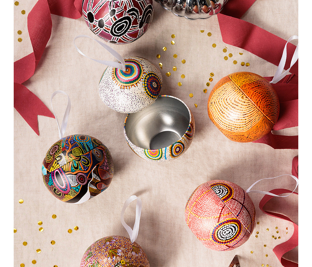 Aboriginal Art Christmas ornaments on a textured surface with ribbons and confetti.
