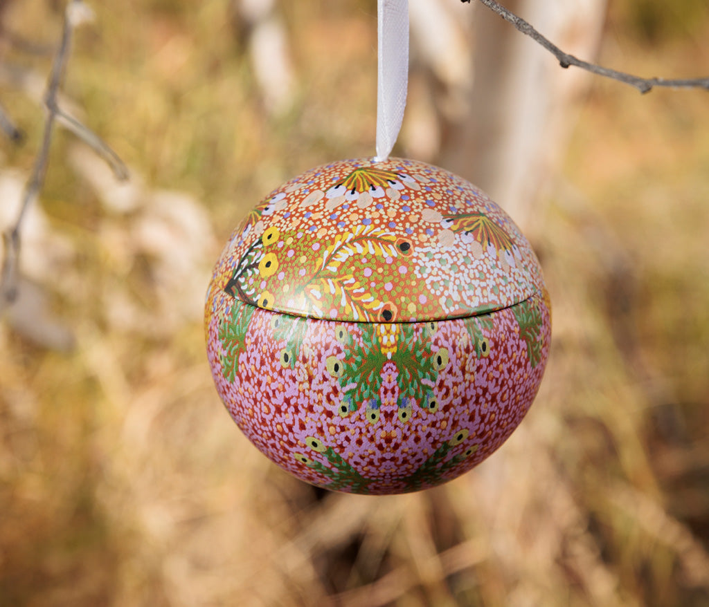 Sandra Pula Teece Aboriginal Art Christmas Bauble hanging from a tree branch outdoors.