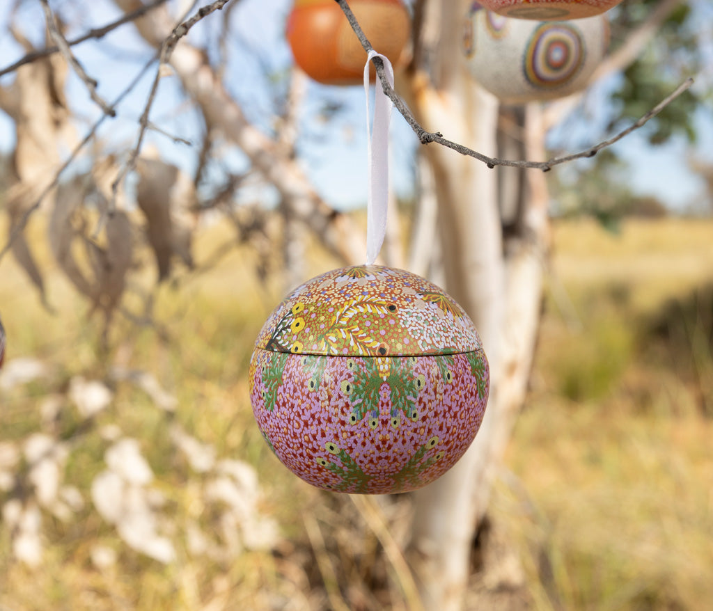 Sandra Pula Teece Aboriginal Art Christmas Bauble hanging from a tree branch outdoors.