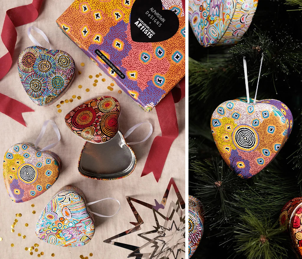 A split image showing Aboriginal Art heart-shaped patterned ornaments and their colorful packaging. The left side shows several heart ornaments, alongside an open heart-shaped box and ribbons on a beige surface.
