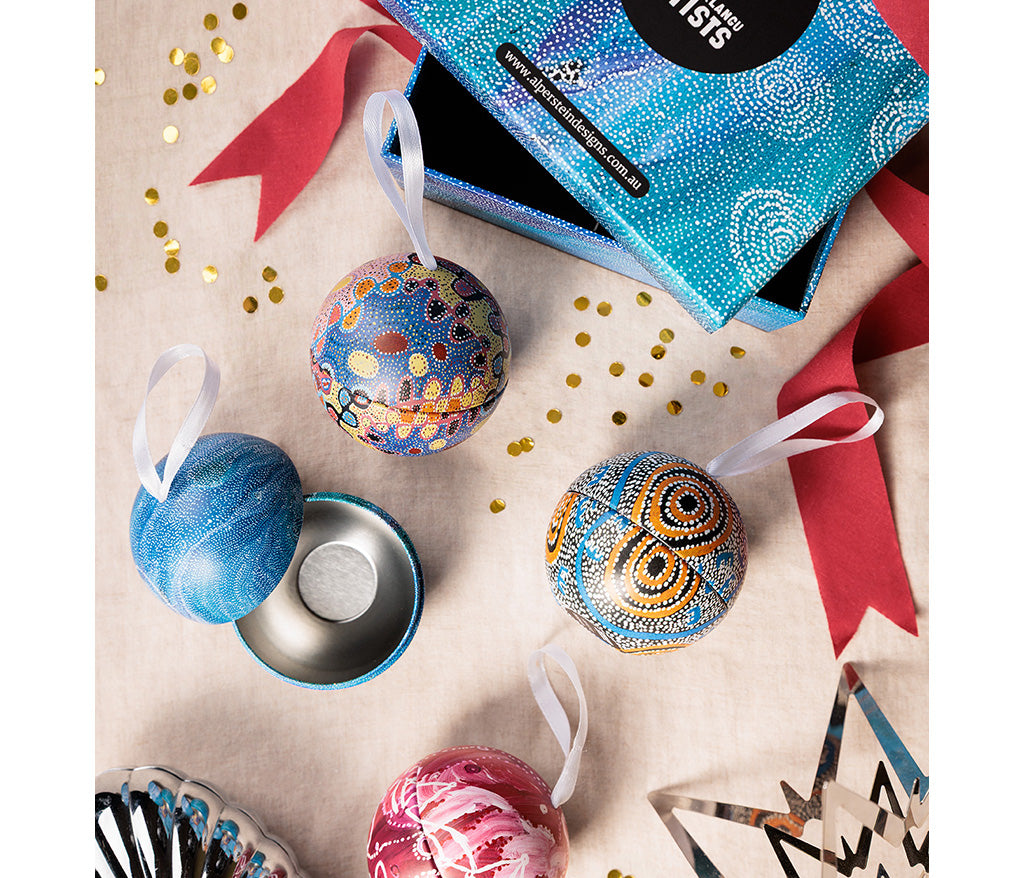 Aboriginal Art Christmas ornaments and packaging on a decorative surface with ribbons and confetti.