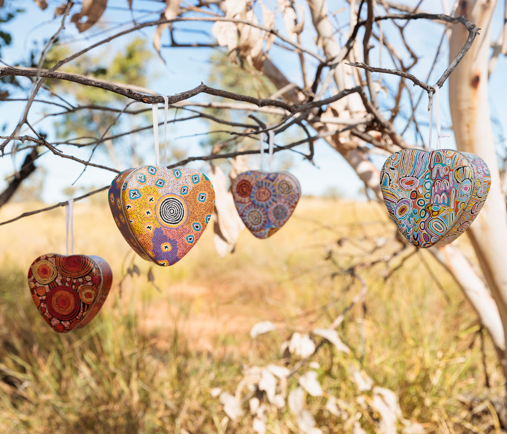 Aboriginal Art heart-shaped decorations hanging from a tree in an outdoor setting.